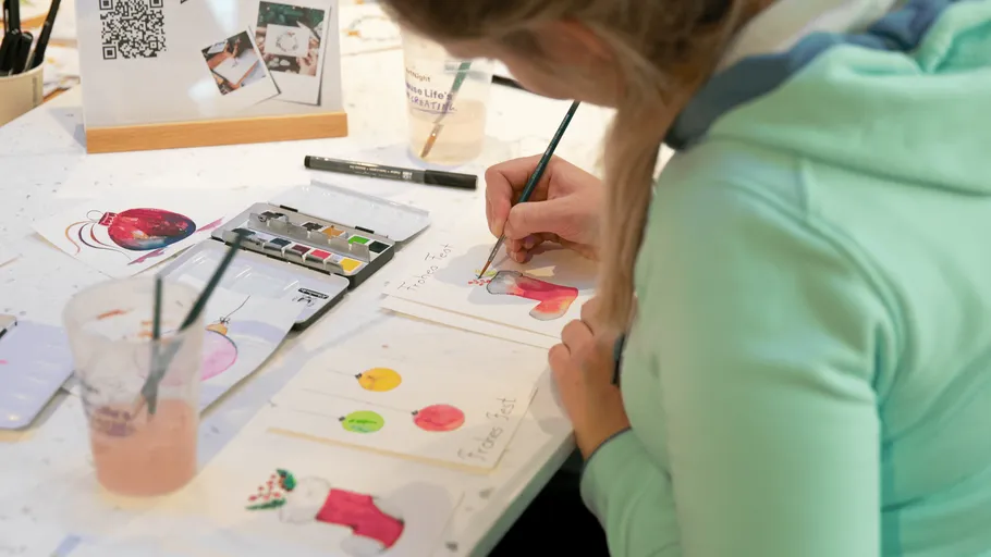 Person painting Christmas-themed cards at table.