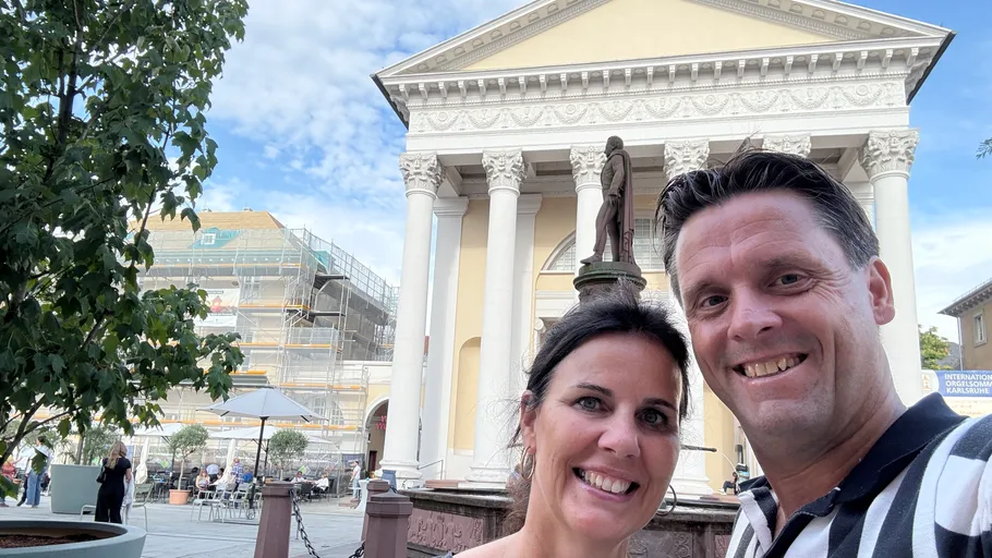 Two people smiling in front of a neoclassical building.