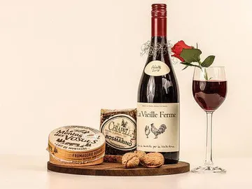 Rotwein und Käse auf einem Holzbrett, Rose daneben.