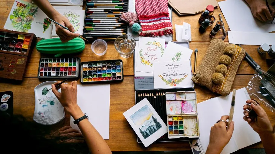 Personen malen mit Aquarellfarben am Tisch.