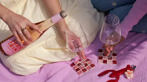 Two people holding wine glasses on picnic blanket.
