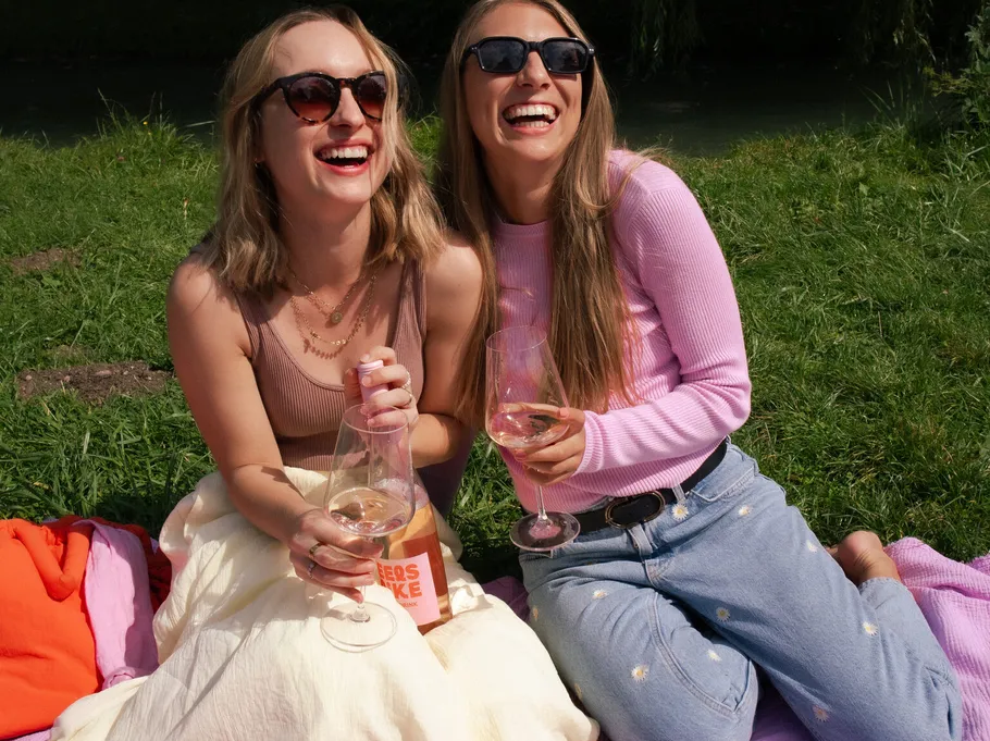 Zwei Frauen lachen mit Wein im Freien.