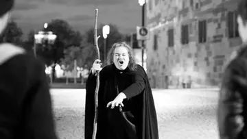 Person with staff gestures dramatically outdoors at night.
