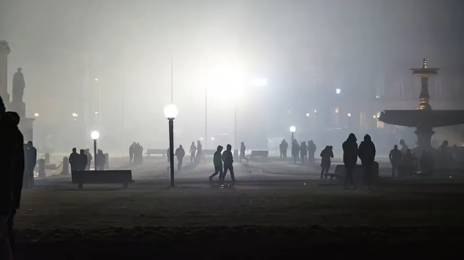 People walking in foggy park at night.