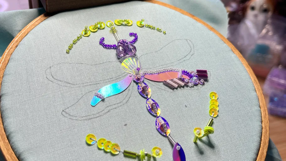 Beaded dragonfly being embroidered on fabric.