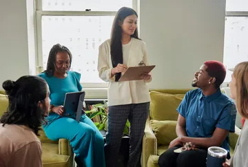Group in meeting, woman holding clipboard.