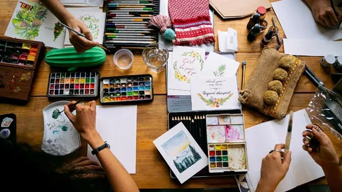 Artists painting on a cluttered wooden table.