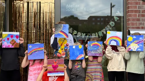 Children holding paintings, standing outside art studio.