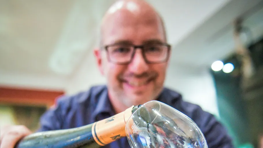 Man smiling holding a wine bottle indoors.