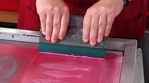 Hands holding squeegee for screen printing fish.