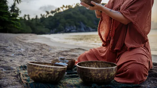 Woman playing singing bowls on beach.