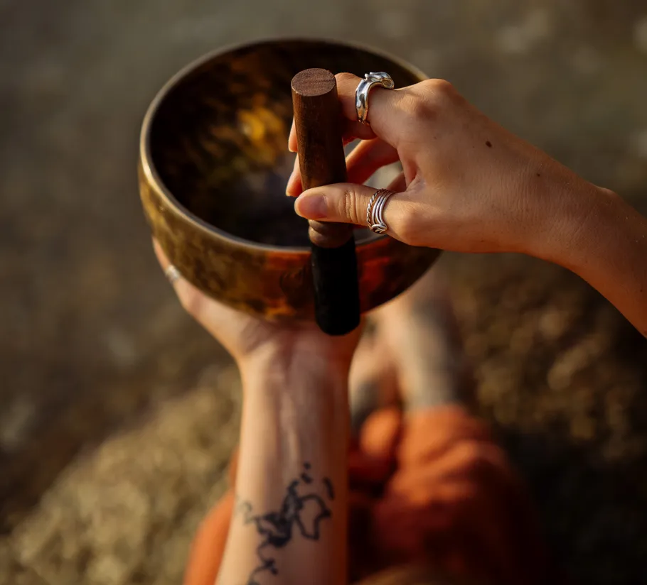 Hand striking a singing bowl outdoors.