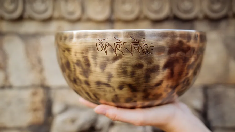 Decorative bowl held against ornate stone background.