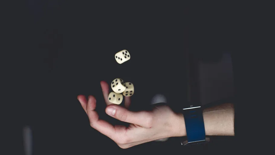 Hand jongliert Würfel vor dunklem Hintergrund.