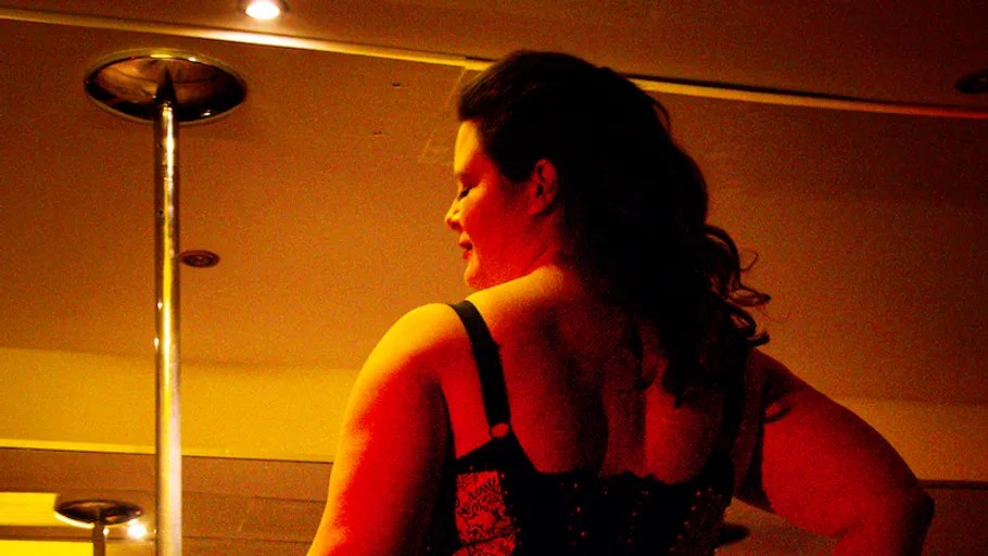 Woman posing beside pole in dimly lit room.