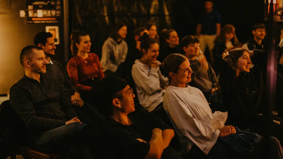 Group of people sitting, watching something, indoors.