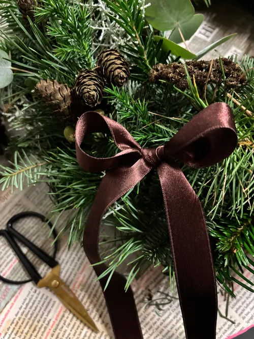 Pine branches with ribbon and scissors on newspaper.