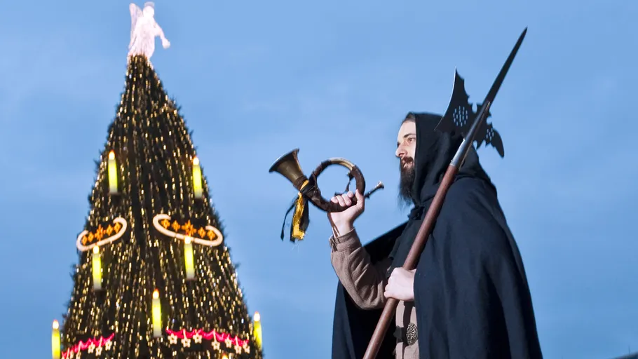 Mann hält Horn neben beleuchtetem Weihnachtsbaum.