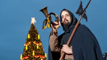 Person hält Horn vor geschmücktem Baum.