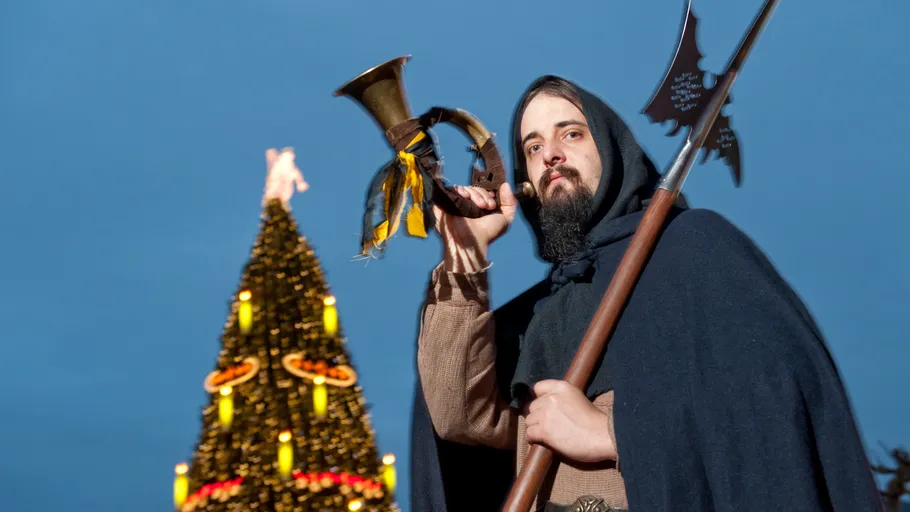 Person hält Horn vor geschmücktem Baum.