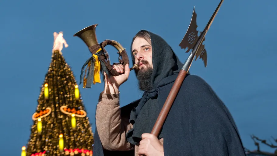 Person bläst Horn neben geschmücktem Baum.