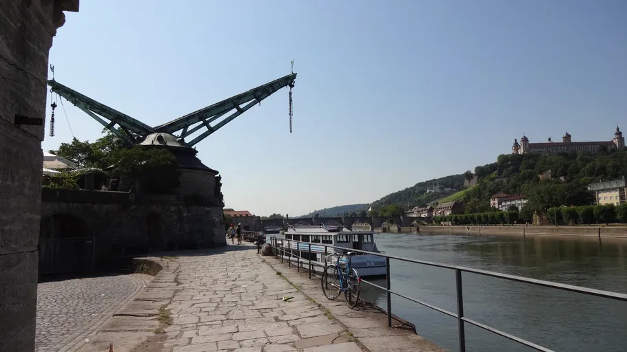 Medieval crane by river with fortress hill.