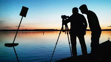Two photographers at sunset by lake.