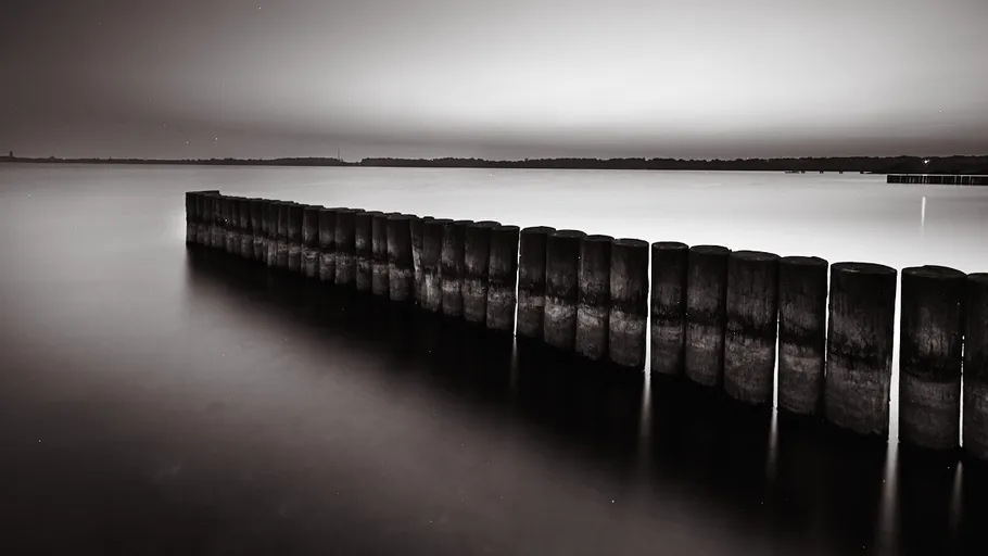 Wooden poles stretching into calm, misty water.