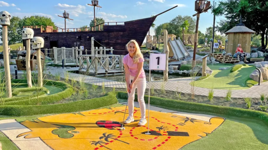 Person playing mini-golf on pirate-themed course.