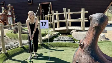 Person spielt Minigolf neben Piratenschiff.