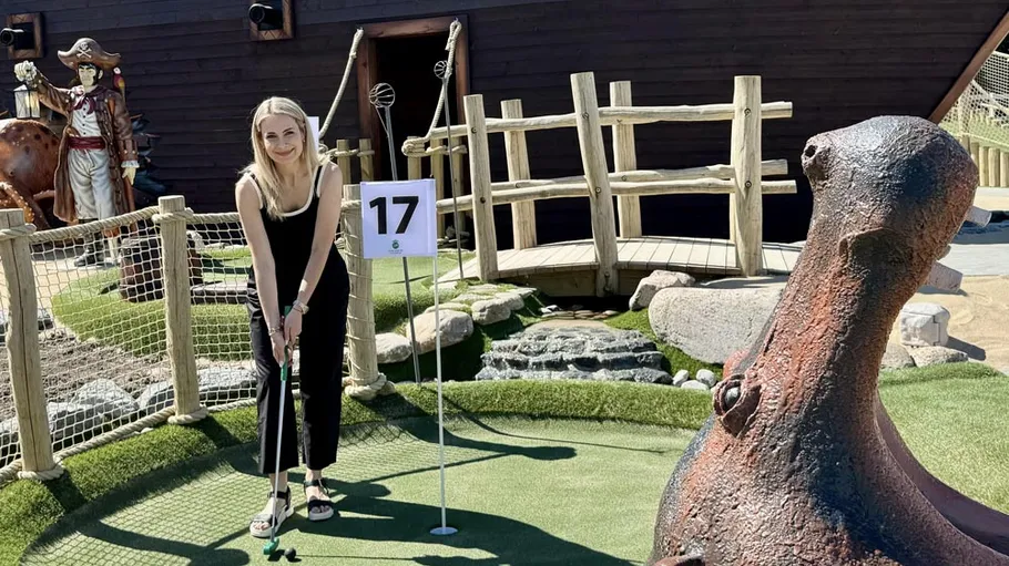 Person playing mini golf beside pirate ship.