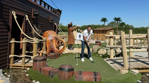 Man playing mini-golf near pirate ship setting.