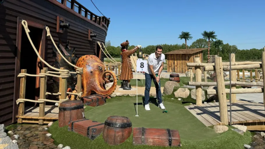 Mann spielt Minigolf neben Piratenschiff-Szene.