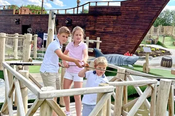 Kinder spielen Minigolf neben Holzschiff.