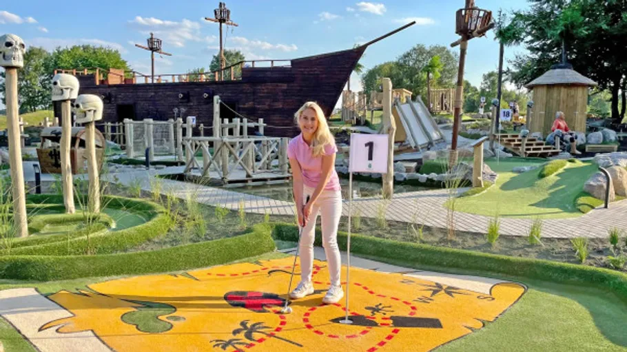 Frau spielt Minigolf vor Piratenschiff.