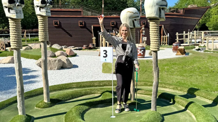 Woman celebrates mini-golf win near pirate ship.