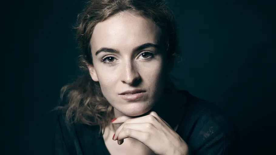 Woman looking at camera, hand on chin, dark background.