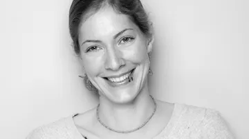 Woman smiling, wearing earrings, neutral background.