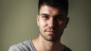 Man smiling softly against plain background.