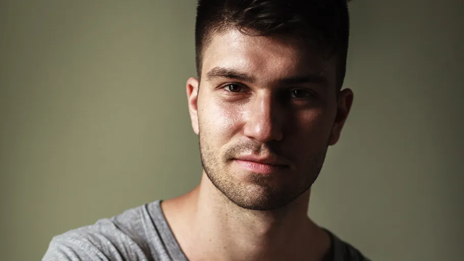 Man smiling softly against plain background.