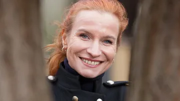 Lächelnde Frau zwischen zwei Bäumen eingerahmt.