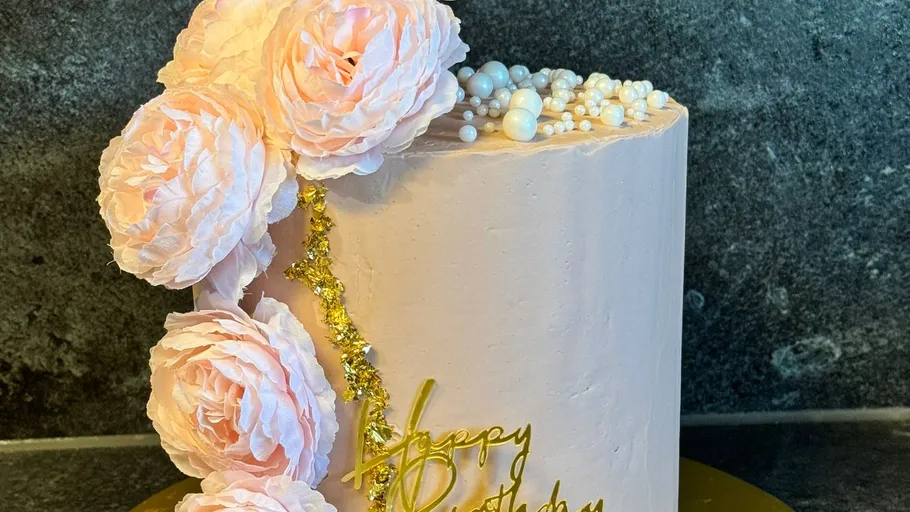 Rosa Kuchen mit Blumen und Dekorationen vor Steinwand.