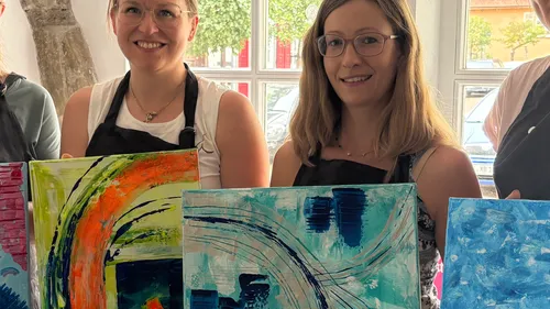Two women holding abstract paintings indoors.