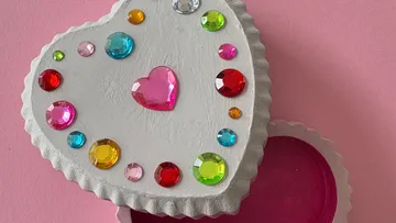 Herzförmige Schachtel mit bunten Edelsteinen, auf Rosa.