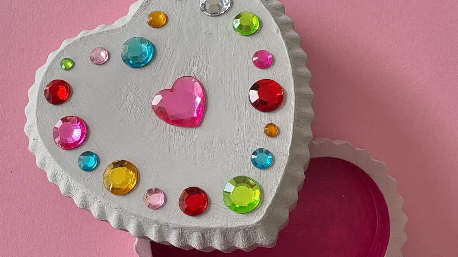 Heart-shaped box with colorful gemstones, on pink.