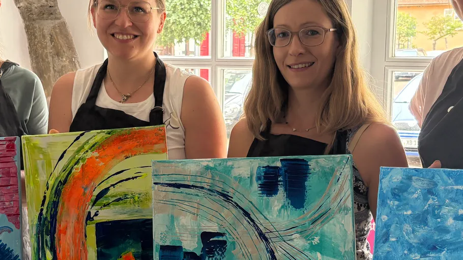 Two women holding abstract paintings indoors.
