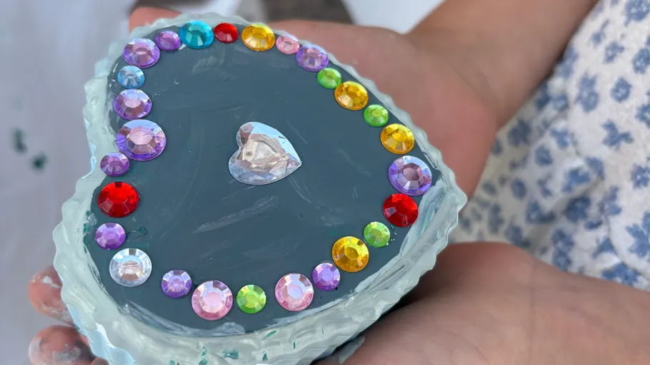 Heart-shaped box with colorful gems held outside.