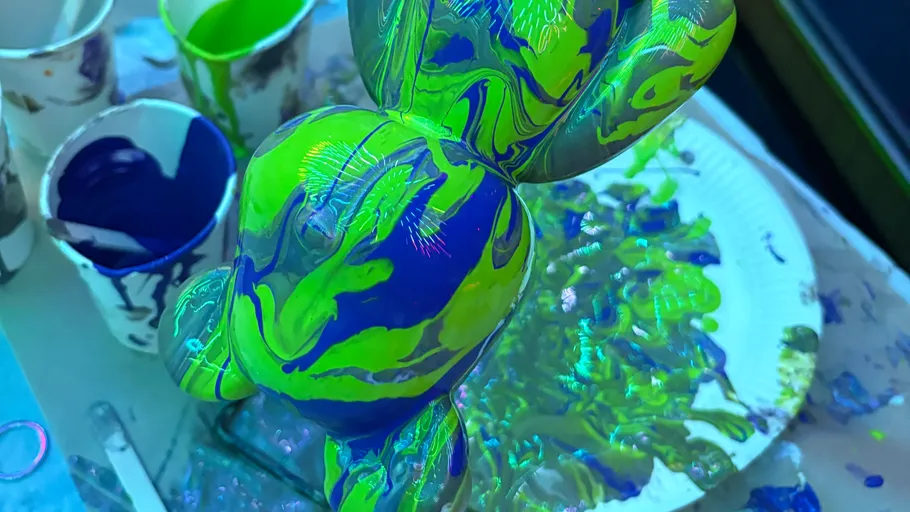 Neonbemalte Skulptur mit Farbbechern und Teller.