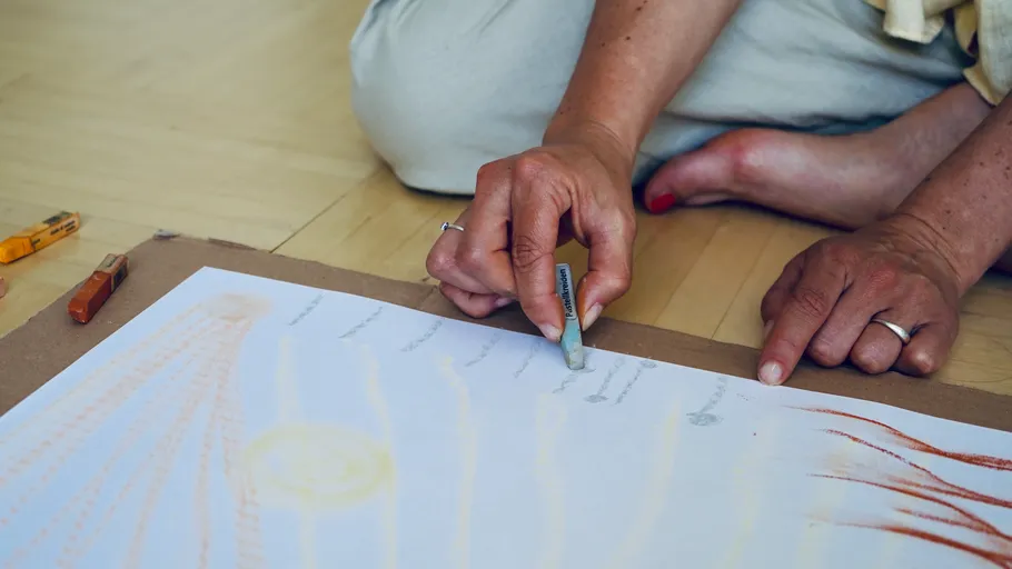 Person drawing with chalk on paper, sitting on floor.