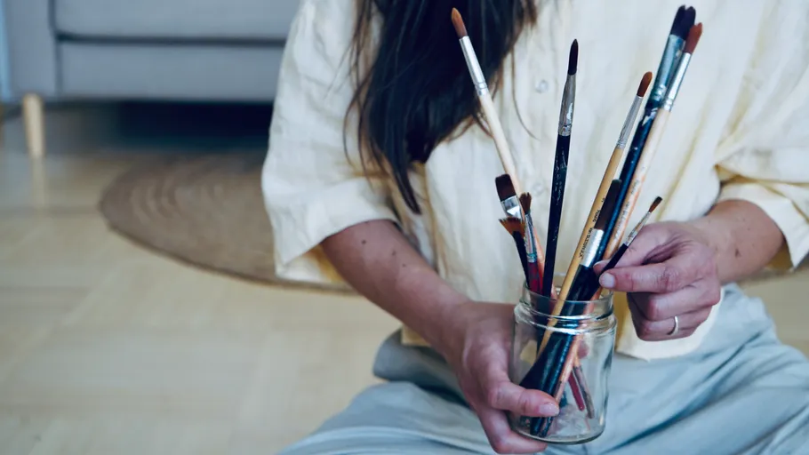Person holding paintbrushes in a jar indoors.